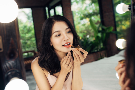 Young beautiful asian woman doing make-up in front of mirrorの写真素材