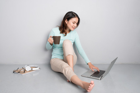 Happy casual beautiful asian woman working on a laptop sitting on floor at home.の写真素材