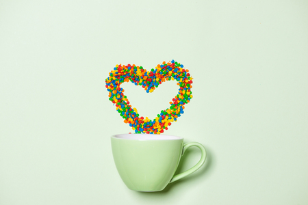 Cup of Cappuccino with heart shape symbol and candy on pastel green backgroundの写真素材