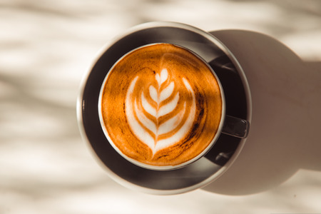 Cup of art latte or cappuccino coffee on table with sunlightの写真素材