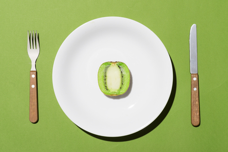 Top view of green kiwi on white plate with knife and fork on green backgroundの写真素材