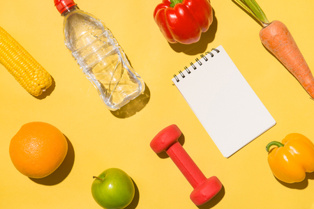 Fitness concept. Collection of fresh fruits with dumbells and water bottle on yellow background.の写真素材