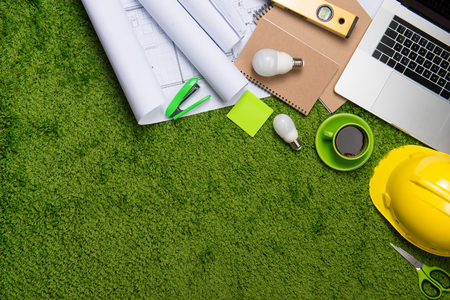 Workplace with helmet, blueprints, laptop and notepad on grass background. Top view with copy spaceの写真素材