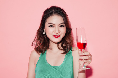 Happy fashion asian woman drinking champagne over pink background.の写真素材