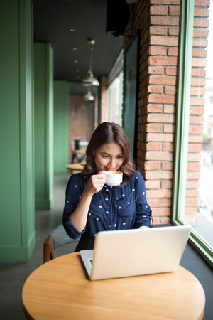 Beautiful cute asian young woman in the cafe, enjoy drinking coffee smilingの写真素材