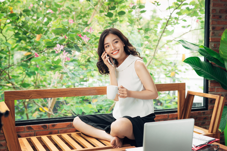 Confident young asian woman in smart casual wear listening to smartphoneの写真素材
