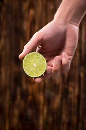 Hand squeeze lime with lime drop on dark wooden backgroundの写真素材