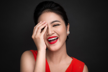 Smiling shy woman closed her face with a hand over black background.の写真素材