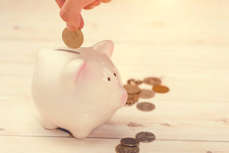 Hand putting golden coins into a pink piggy bank. Japanese Yen.の写真素材