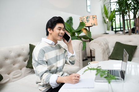 Asian businessman using mobile phone while working with laptop on table in coffee shopの写真素材