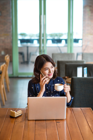 Beautiful cute asian young businesswoman in the cafe, listening to mobile phone and holding coffee mugの写真素材