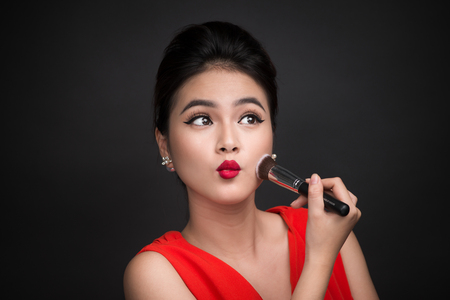 Cosmetic powder brush. Asian woman applying blusher on her cheeks with perfect make-up and red lipsの写真素材