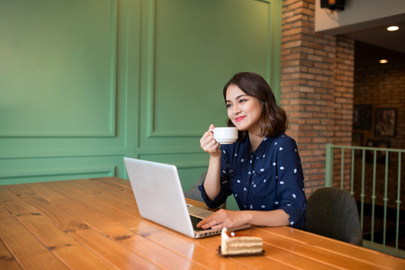 Beautiful cute asian young businesswoman in the cafe, using laptop and drinking coffee smilingの写真素材