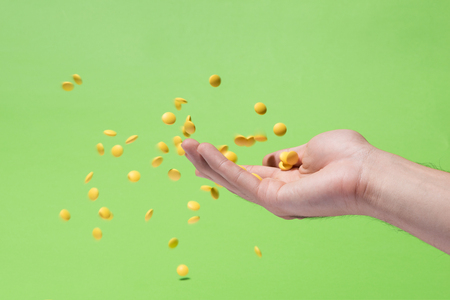 Flying yellow pills from hand in front of green backgroundの写真素材