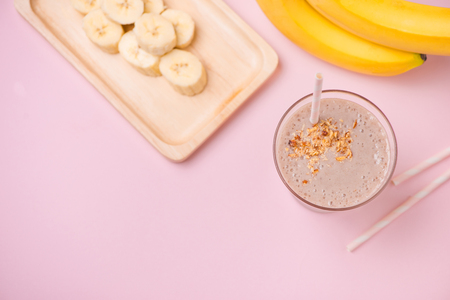 Fresh made banana smoothie in a glass on pink backgroundの写真素材