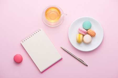 Flatlay of notebook, cake macaron, cup of tea and flower on pink table. Beautiful breakfast with macaroon.の写真素材