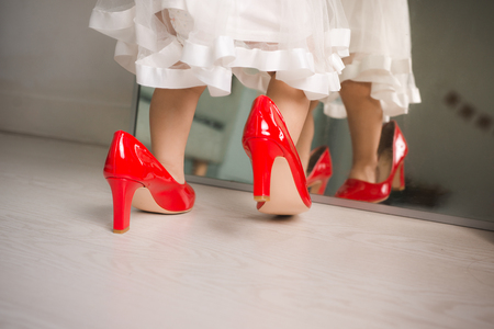 Cute funny little baby girl walks at home trying mom's red high heel shoesの写真素材