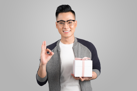 Portrait of asian young man holding gift box isolated over gray backgroundの写真素材