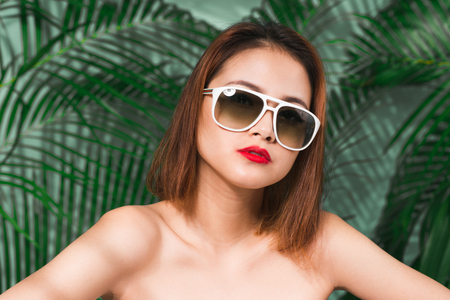 Colorful portrait of young attractive asian woman in sexy dress and wearing sunglasses over blue background. Summer beauty conceptの写真素材
