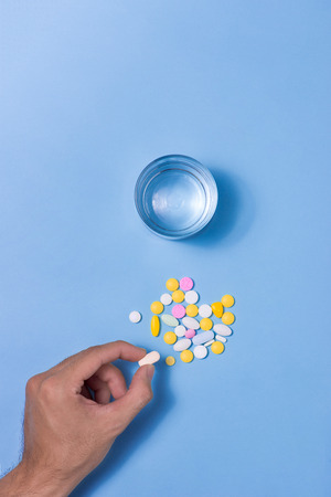 Colored pills in hand with water on blue background.の写真素材