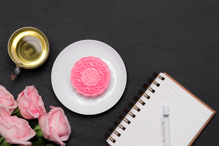 Snow skin mooncake and tea cup with flowers on dark background. Open notebook with copy-space.の写真素材
