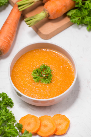 Carrot soup with cream and parsley on white stone background. Top view. Copy spaceの写真素材
