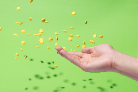 Flying yellow pills from hand in front of green backgroundの写真素材