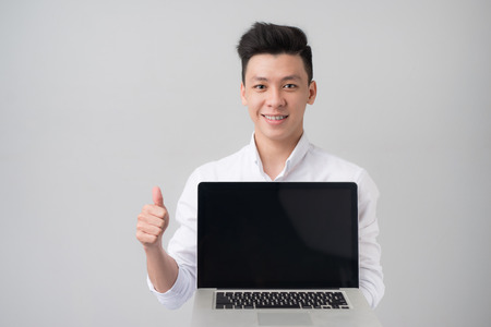 Young asian man in casual clothes holding and showing screen of laptopの写真素材