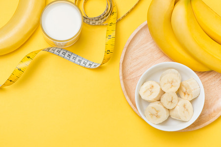 Bananas and milk glass with measuring tape on yellow background with copy spaceの写真素材