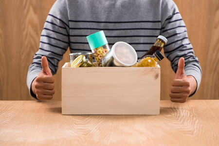 Volunteer with donation box with foodstuffs on wooden backgroundの写真素材