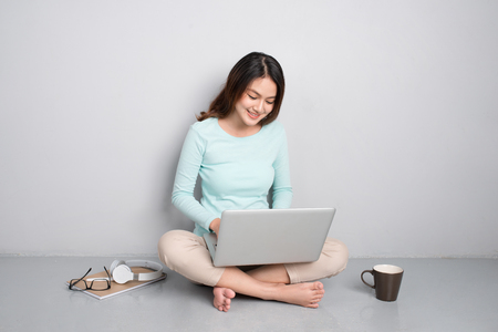 Happy casual beautiful asian woman working on a laptop sitting on floor at home.の写真素材