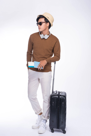 Full length of young asian man holding passport with suitcase over grey backgroundの写真素材