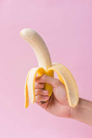 Male hand holding peeled banana isolated on pink background.の写真素材