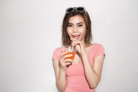 Beautiful young girl model stands on white background in sexy bathing suit with wet hair drinking orange juiceの写真素材