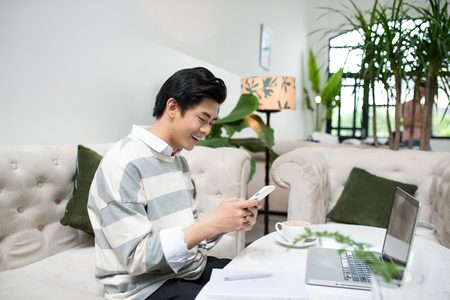 Asian male student texting by phone while sitting at the cafe shopの写真素材