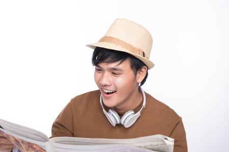 Smart casual asian man seated on chair, reading newspaper in studio backgroundの写真素材