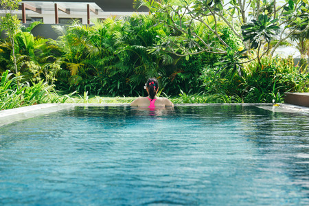 Young woman enjoyng sunny day in luxury pool. Relaxing, tropical, vacationの写真素材