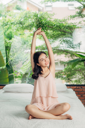Asian woman stretching sitting on bed in the morningの写真素材