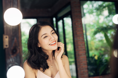 Pretty happy asian woman watching on herself in a big mirror at home.の写真素材