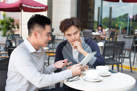 Two young handsome businessmen in casual clothes smiling, talking in coffee shop.の写真素材
