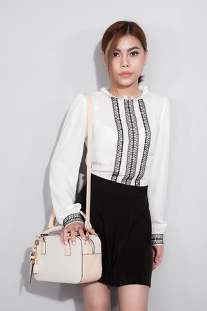 Full-length portrait of beautiful asian woman holding a bag walking over gray background.の写真素材