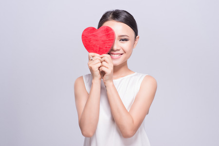 Beautiful young asian woman holding red heart on whiteの写真素材