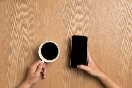 Man using smart phone sitting on table, hand holding smart phone showing screen.の写真素材