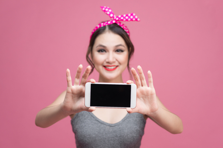 Beautiful young asian woman with pin-up make-up and hairstyle over pink background with mobile phoneの写真素材