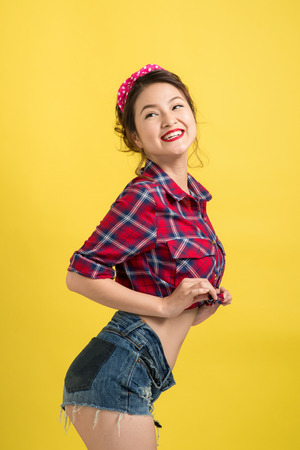 Asian woman retro portrait with pin-up make-up and hairstyle posing over yellow background.の写真素材