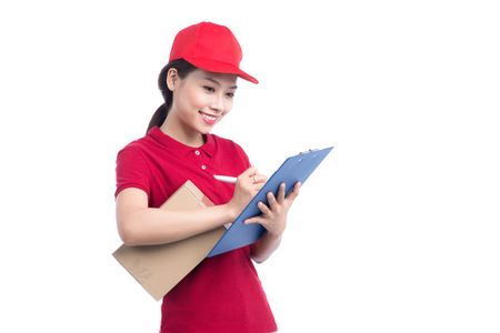 Beautiful young delivery woman in red t-shirt and cap smiling, holding a folder and making notes, on white backgroundの写真素材