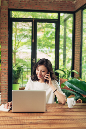 Confident smiling asian woman using phone and laptopの写真素材