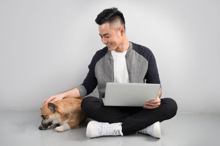 Handsome young businessman is using laptop while sitting with his dog o chairの写真素材