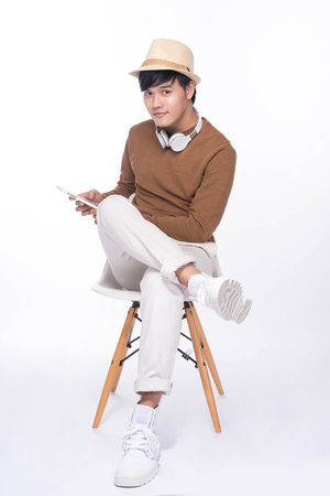 Smart casual asian man seated on chair, holding smartphone in studio backgroundの写真素材