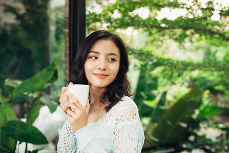 Pretty vietnamese woman enjoying her morning coffee on a verandaの写真素材